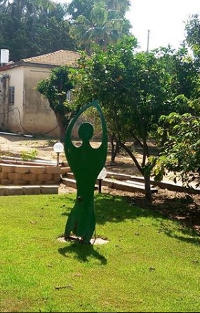 פיגורה של אישה ממתכת ירוקה ניצבת במדשאה